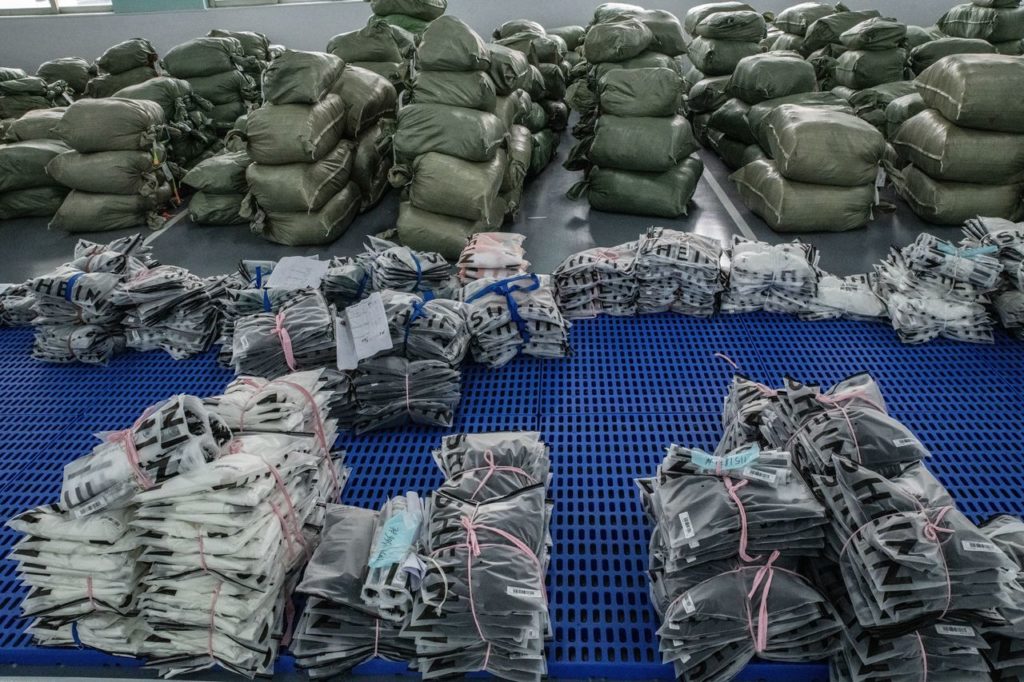 Inúmeros sacos empilhados e produtos embalados, alguns da SHEIN, em um centro de distribuição.
