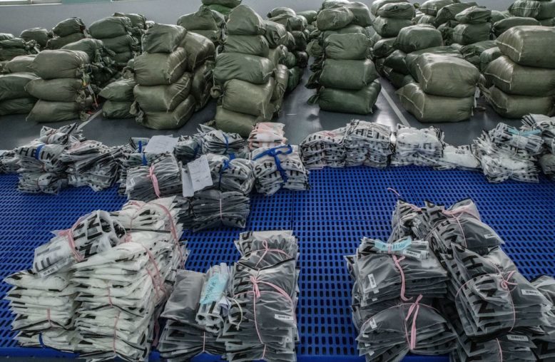 Inúmeros sacos empilhados e produtos embalados, alguns da SHEIN, em um centro de distribuição.