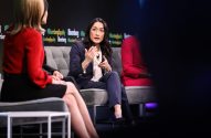 Mulher em painel da Bloomberg gesticula ao falar, outras participantes sentadas em um sofá no palco.