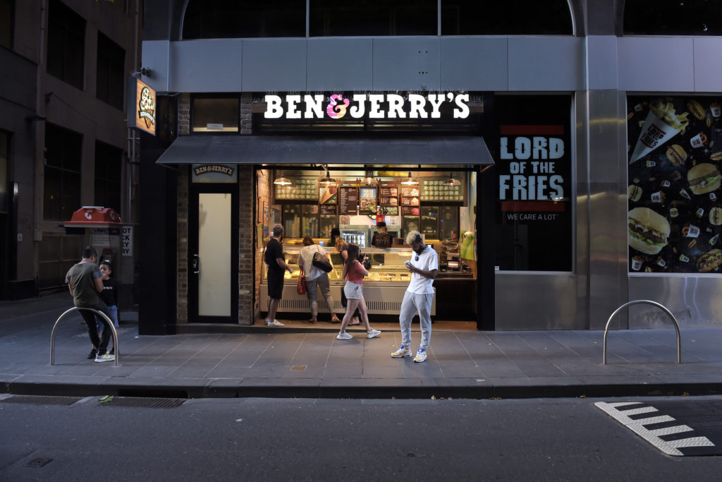 Fachada de loja Ben & Jerry's em rua urbana. Pessoas na calçada e perto da entrada da loja.