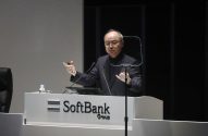 Homem discursa em pódio branco com logo "SoftBank Group", gesticulando com as mãos.