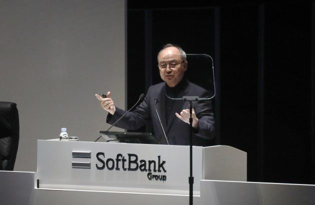 Homem discursa em pódio branco com logo "SoftBank Group", gesticulando com as mãos.