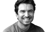 Homem sorridente em foto de rosto monocromática.