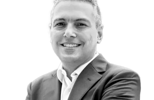 Retrato profissional em preto e branco de homem sorrindo com braços cruzados.