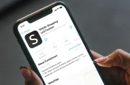 Mão segurando smartphone aberto na página de download do aplicativo do e-commerce de roupas Shein