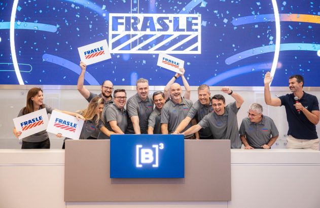 Pessoas comemorando em frente a telão 'FRASLE', segurando placas FRASLE. No pódio, logo [B]³.