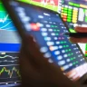 um tablet e duas telas de computador mostrando gráficos de ações de tecnologia na bolsa de valores