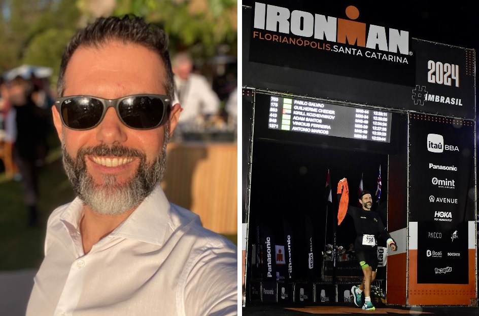 Homem sorrindo de óculos e estande IRONMAN com telas de informações.