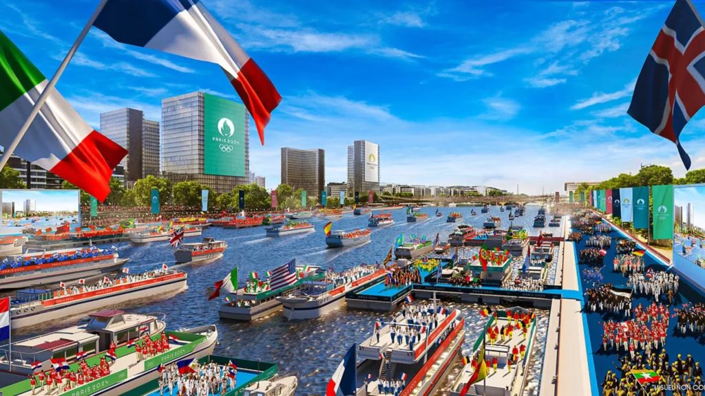 Abertura Olímpica Paris 2024: desfile de barcos no rio, pessoas nas margens e bandeiras nacionais.