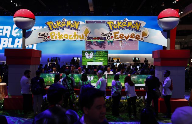 Evento Pokémon: Pessoas jogam Let's Go Pikachu/Eevee em estandes com grandes Poké Bolas e monitores de jogo.