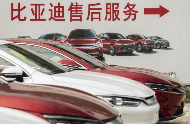 Carros BYD vermelhos e brancos com banner de "Serviço Pós-Venda BYD" e seta direcional.