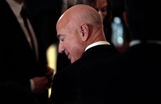 Jeff Bezos, de perfil, com cabeça baixa, em traje formal escuro.