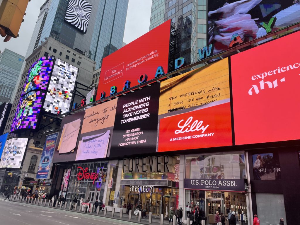 Vista diurna da Times Square com pessoas caminhando e muitos outdoors digitais exibindo anúncios.