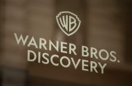 Logotipo e nome da Warner Bros. Discovery em destaque numa porta de vidro.