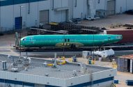 Fuselagem de avião verde em pátio industrial.