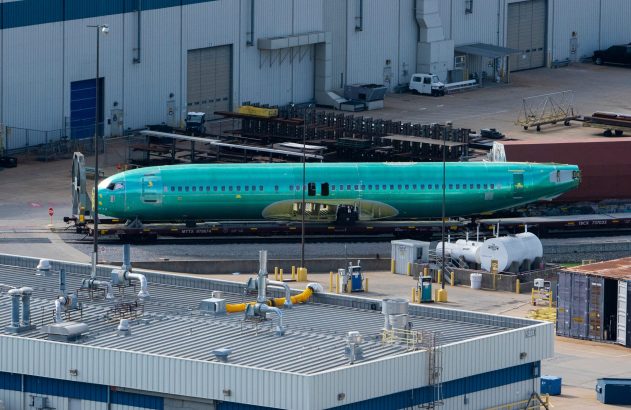 Fuselagem de avião verde em pátio industrial.