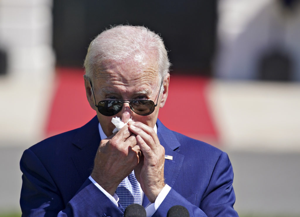 Joe Biden, de óculos escuros e terno azul, assoando o nariz com um lenço de papel.