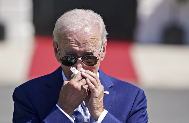 Joe Biden, de óculos escuros e terno azul, assoando o nariz com um lenço de papel.