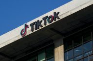 Logotipo "TikTok" em preto, ciano e rosa na fachada de concreto de um edifício contra céu azul.