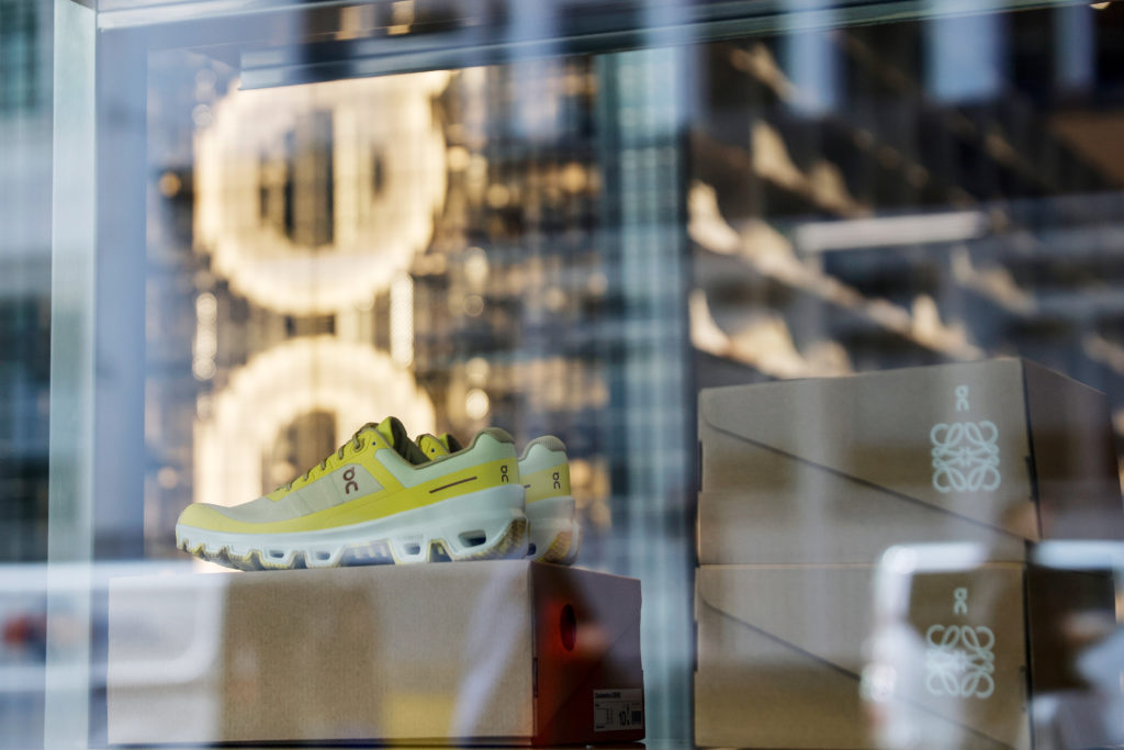 Um tênis esportivo On amarelo e branco em vitrine. Caixas Loewe e On (colaboração) empilhadas à direita.