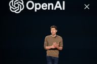Palestrante gesticula em palco escuro com logo OpenAI no fundo.