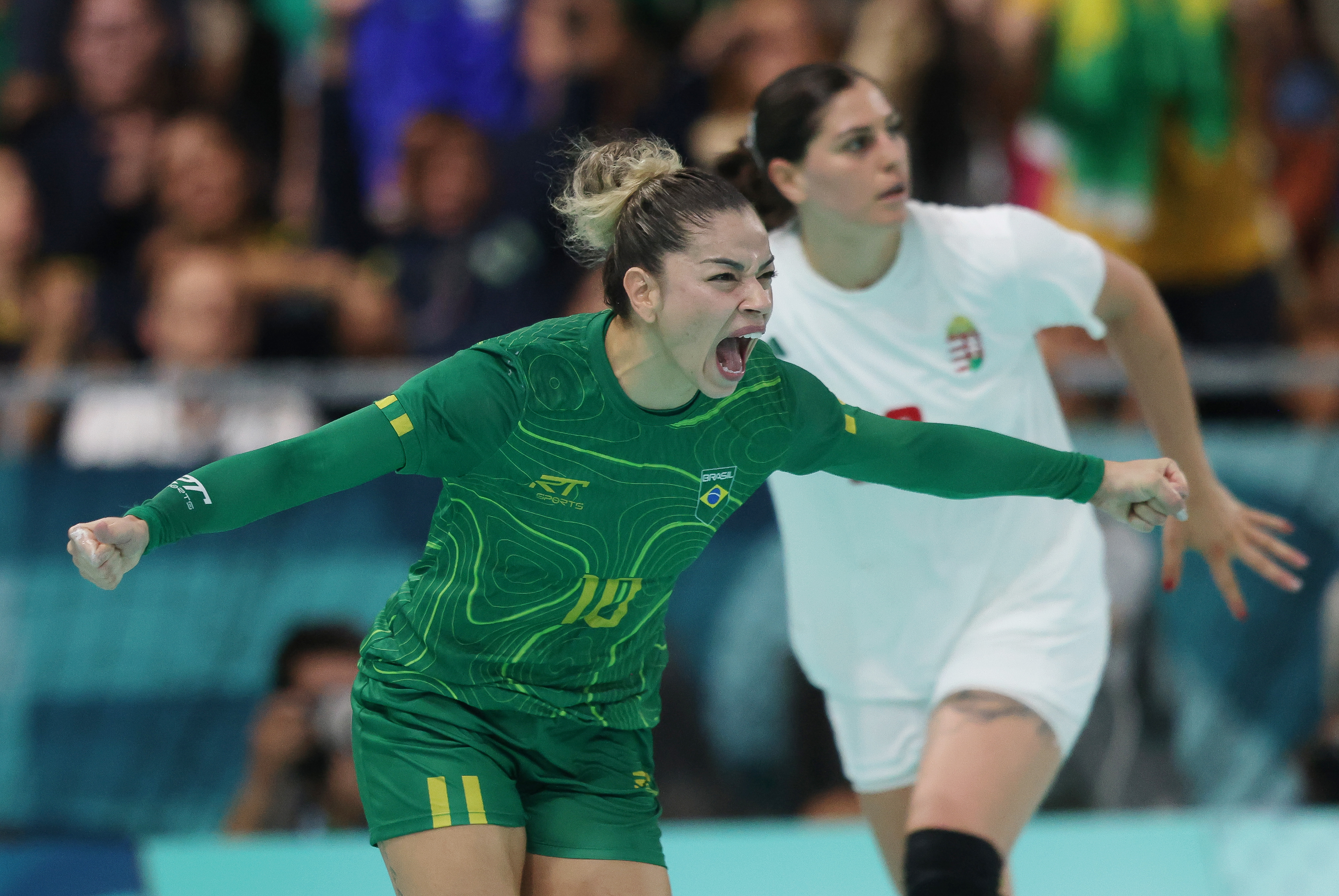 Atleta de verde do Brasil comemora gritando. Atleta de branco da Hungria ao fundo.