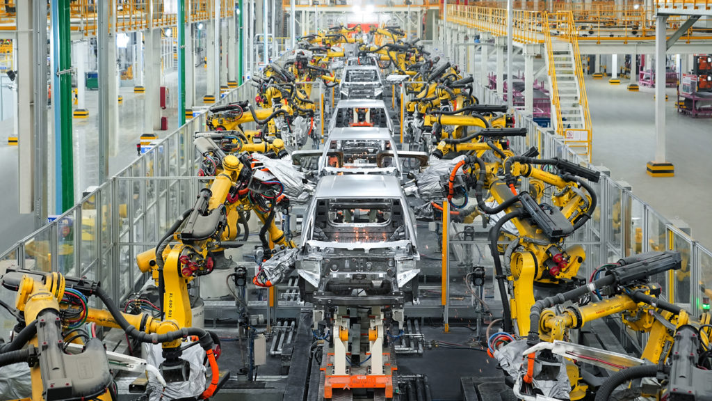 Braços robóticos montam veículos em uma linha de produção automotiva. Indústria moderna e automatizada.