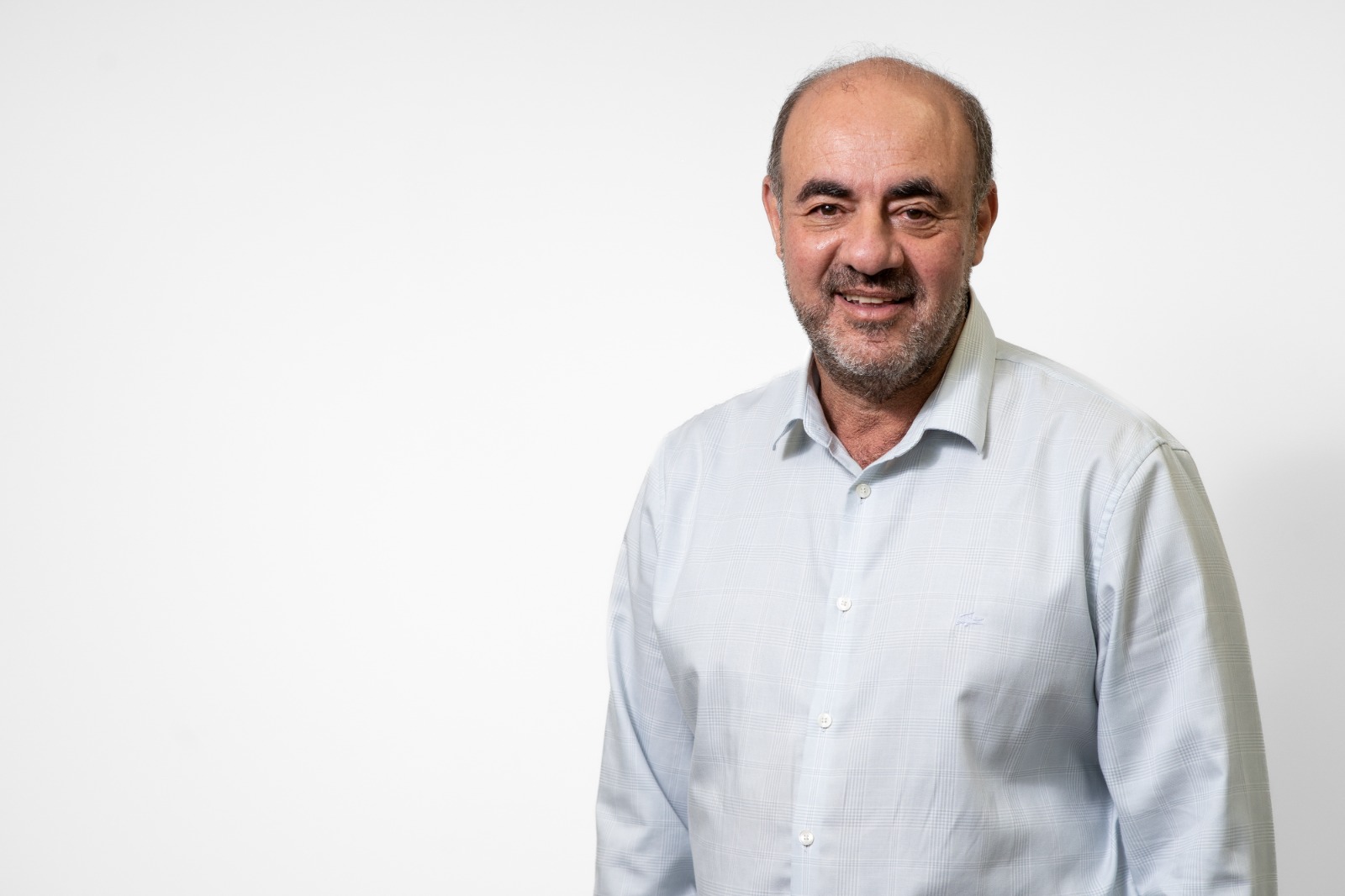 Homem sorridente de camisa azul em fundo branco olhando para a câmera.