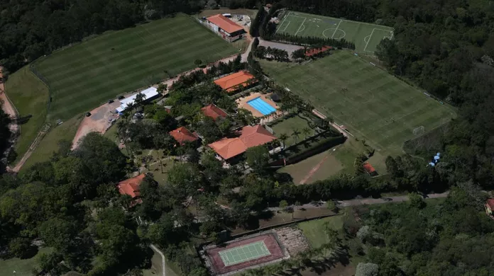 Vista aérea de um complexo esportivo com múltiplos campos de futebol, piscina, edifícios e quadra de tênis.