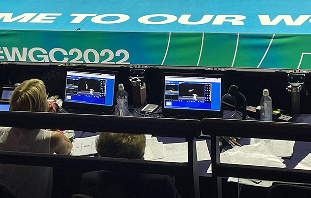 Duas pessoas controlam placares em monitores durante um evento com banner "WGC2022".