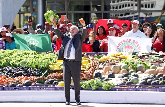 Lula ergue alface e laranja em mesa farta de produtos agrícolas, com público e faixas.