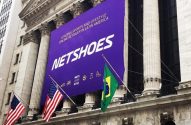 Banner roxo da Netshoes no prédio da NYSE, celebrando a listagem, com bandeiras dos EUA e Brasil.