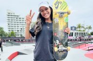 Skatista sorridente fazendo sinal de paz, segurando skate em pista.