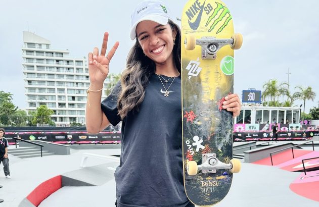 Skatista sorridente fazendo sinal de paz, segurando skate em pista.