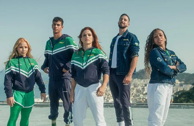 Cinco pessoas em roupas esportivas verde e azul posam ao ar livre com fundo de mar e montanhas.