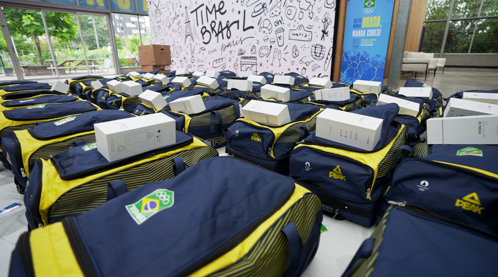 Dezenas de malas esportivas azuis e amarelas com caixas brancas, prontas para o Time Brasil Olímpico.