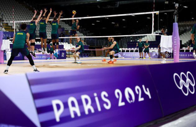 Time de vôlei do Brasil treina em quadra para Paris 2024, com jogadores saltando para ataque e bloqueio.