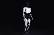 Robô humanoide branco e preto em pé contra fundo escuro.