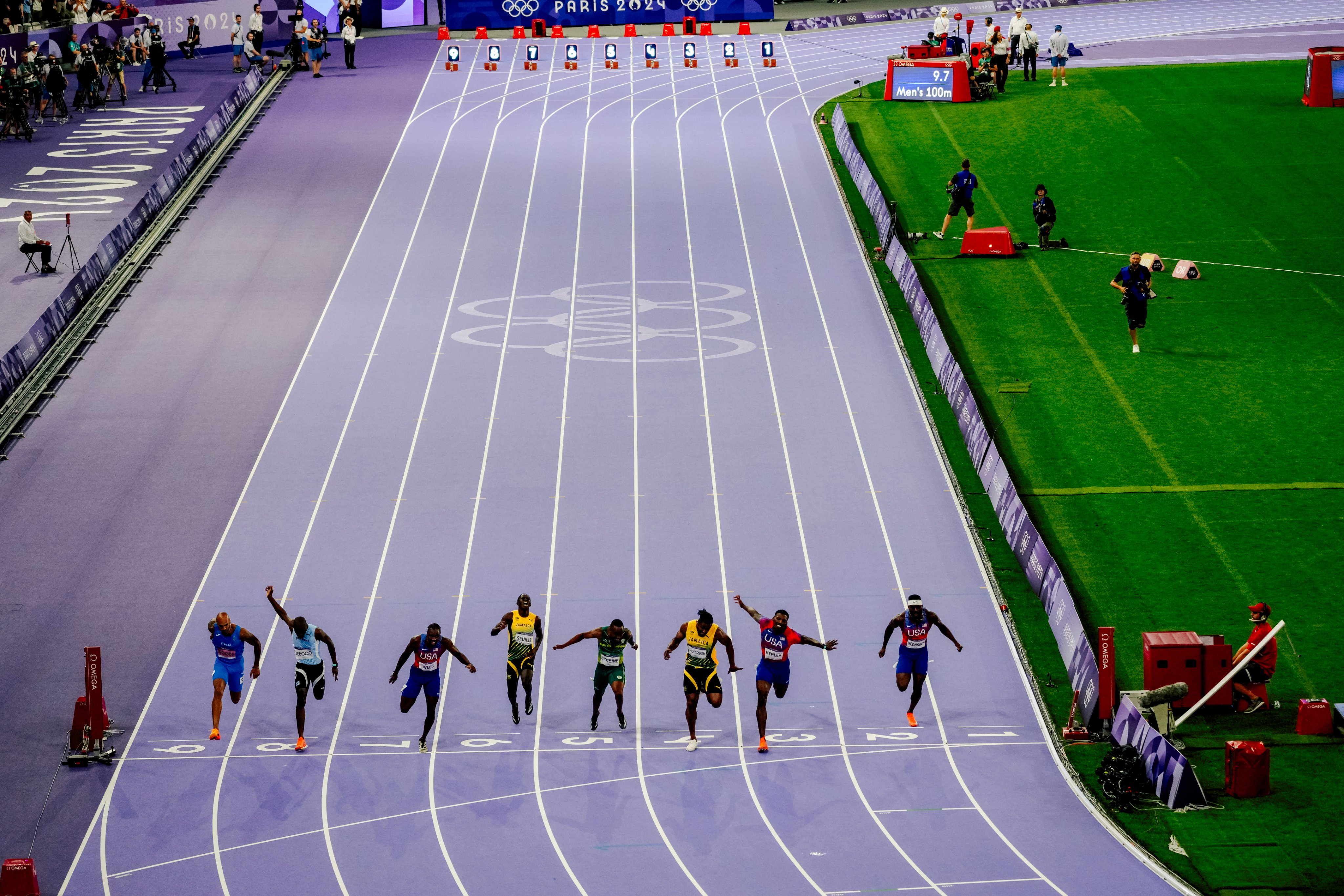 Corredores em blocos de partida na largada de uma prova de atletismo em pista azul.