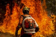Bombeiro com mochila em meio a incêndio florestal intenso.