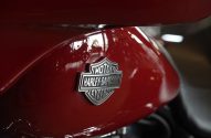 Emblema Harley-Davidson prateado em tanque de moto vermelho com reflexos.