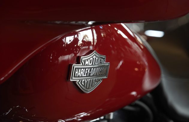 Emblema Harley-Davidson prateado em tanque de moto vermelho com reflexos.