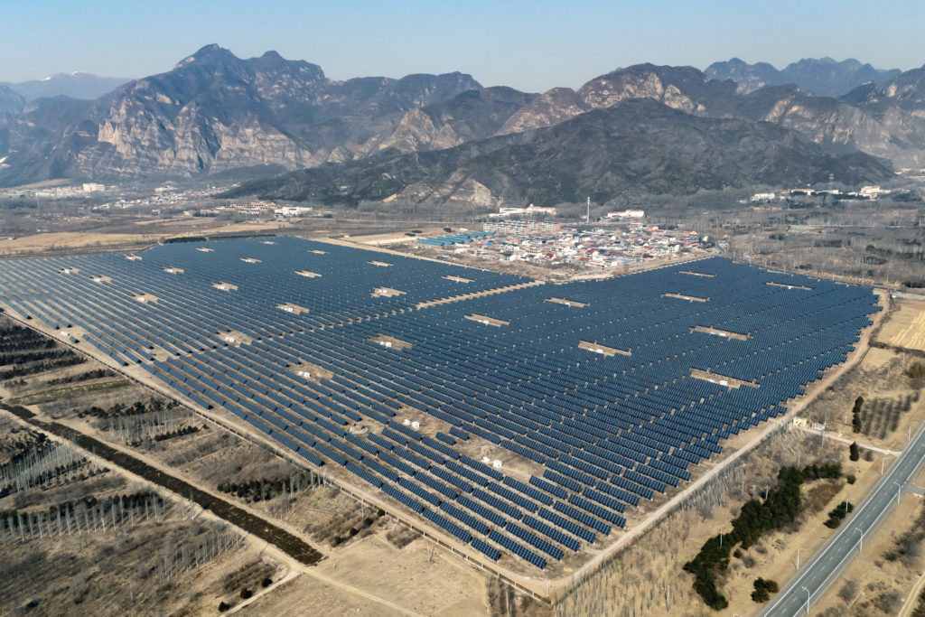 Usina solar em campo aberto com painéis fotovoltaicos e montanhas ao fundo.