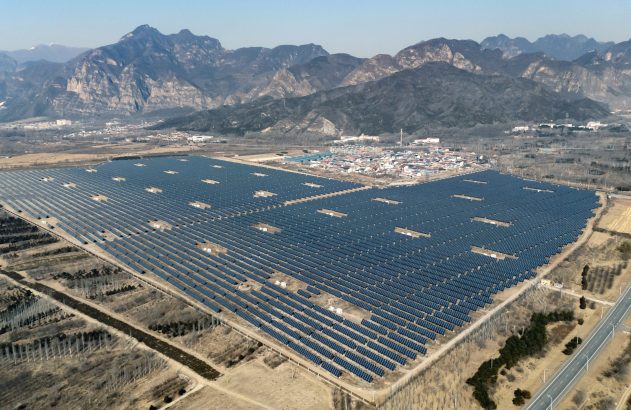 Usina solar em campo aberto com painéis fotovoltaicos e montanhas ao fundo.