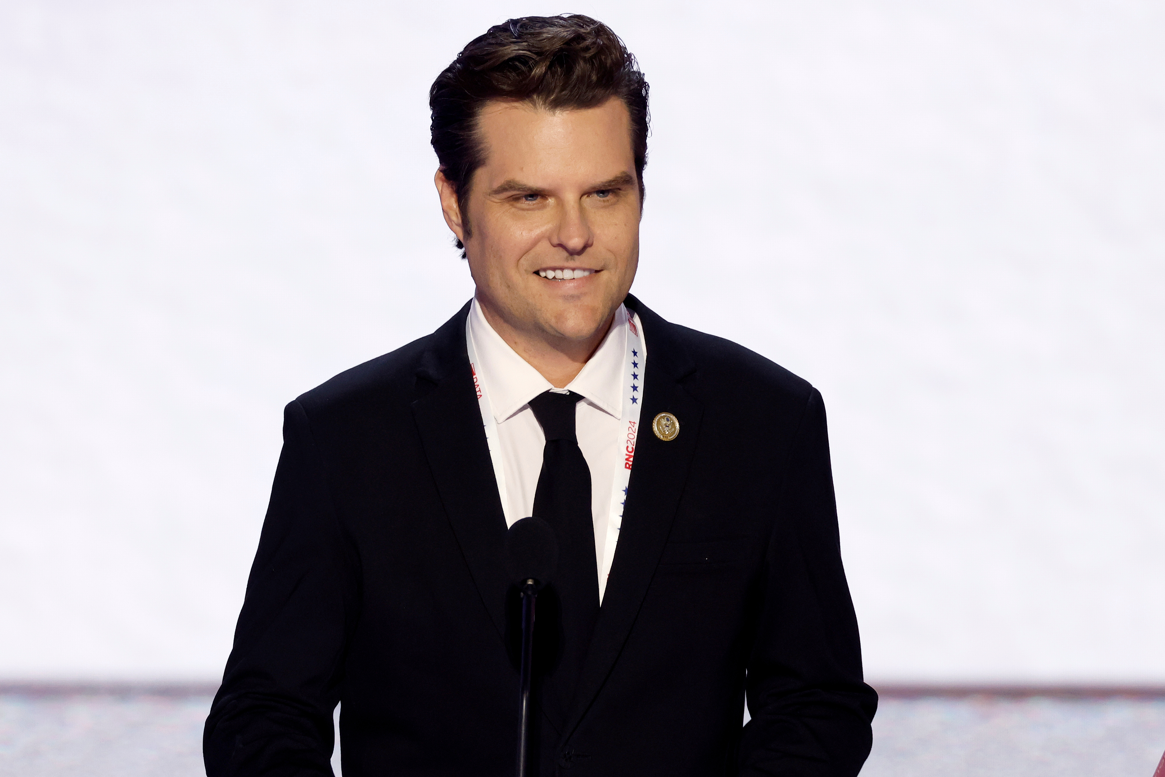 Homem de terno preto sorrindo e falando no pódio de evento RNC 2024.