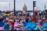 Pessoas assistem ciclistas em corrida, com Invalides e semáforo ao fundo.