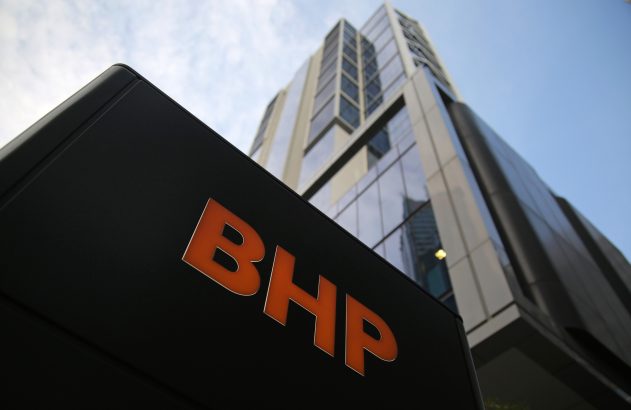Letreiro preto com 'BHP' laranja e um prédio moderno de vidro em perspectiva de baixo para cima.
