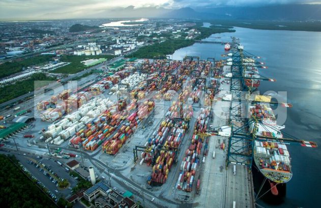 Porto movimentado com navios contêiner atracados e contêineres empilhados. Vista aérea.