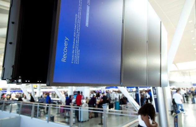 Grande tela digital exibe tela de "Recovery" do Windows, indicando erro de carregamento, em aeroporto.