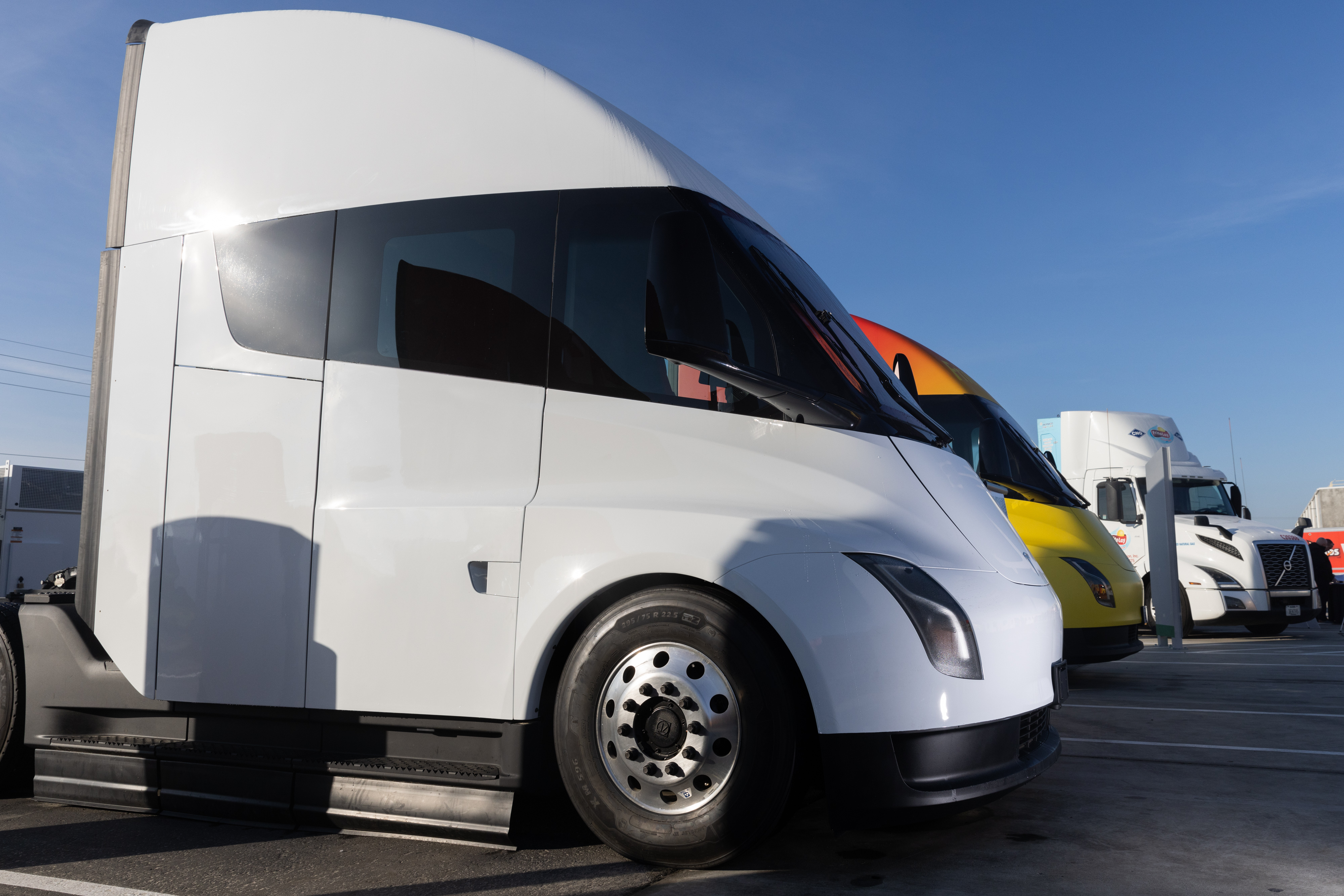Tesla Semi branco estacionado sob o sol, com outros caminhões atrás.